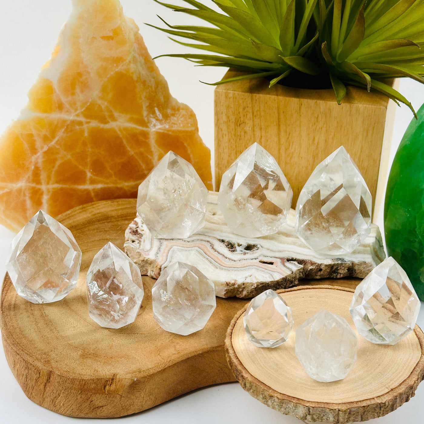 Crystal Quartz Faceted Egg Point - By Weight all weight variants arranged on wood and stone platters with props and plants in background