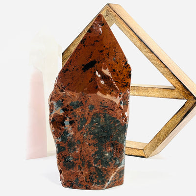 Mahogany Obsidian Crystal Semi Polished Point back view on a white table with a wood shelf and 2 crystal points in the background.