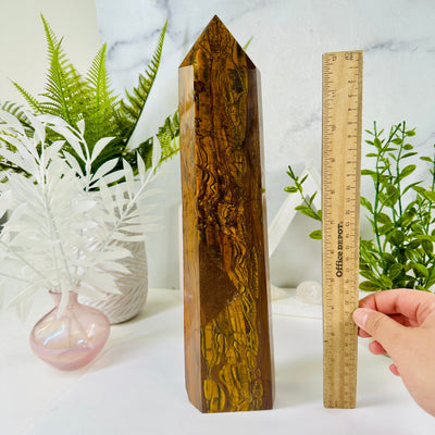 Tigers Eye Crystal Obelisk next to ruler and hand for size reference