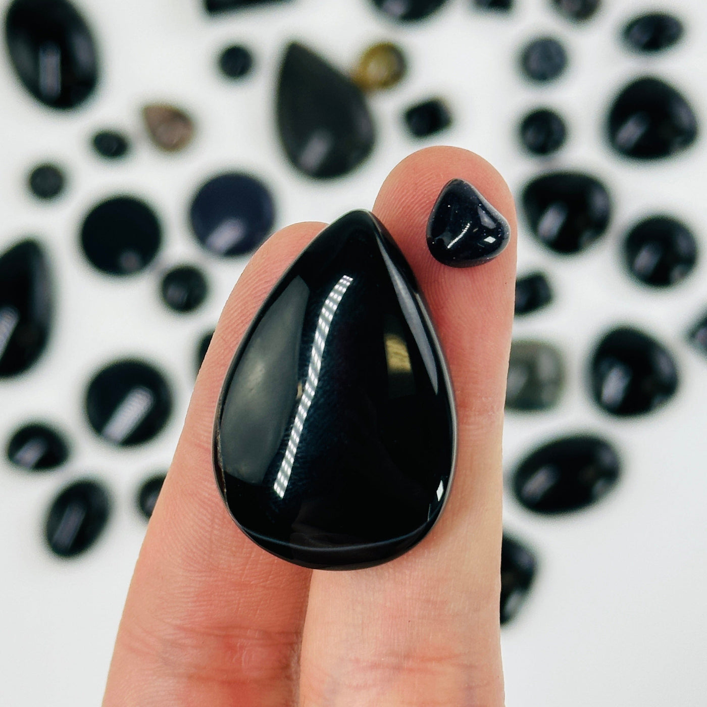 finger holding up black stone cabochons with others in the background