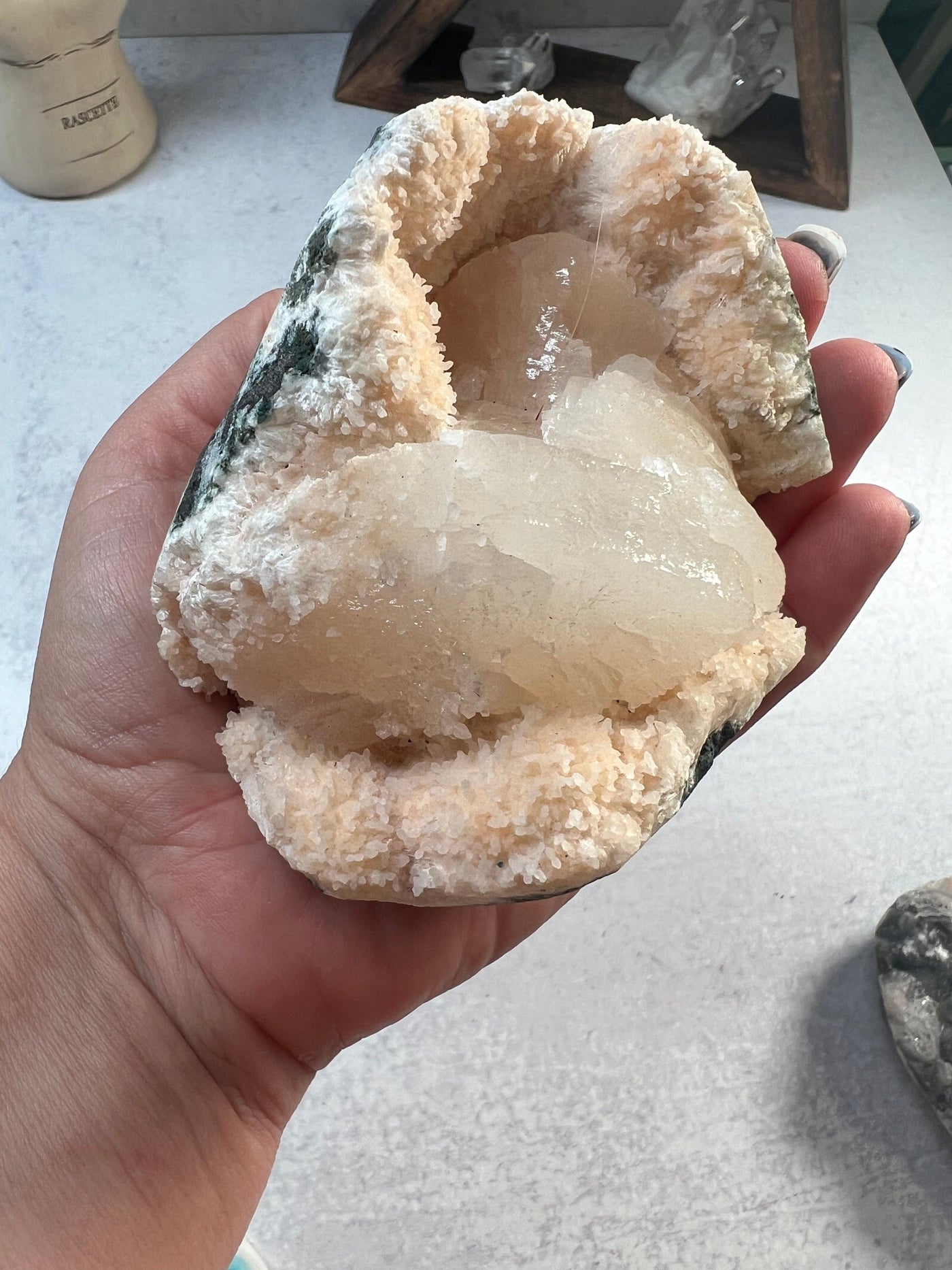 hand holding up stilbite on matrix with decorations in the background