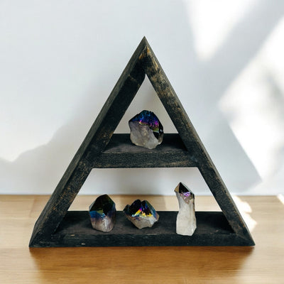 Rainbow Titanium Coated Crystal Quartz Point on a wood shelf on a wood desk with a white wall.