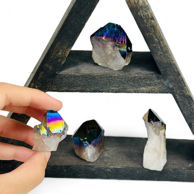 Rainbow Titanium Coated Crystal Quartz Points on a wood shelf with one being held.