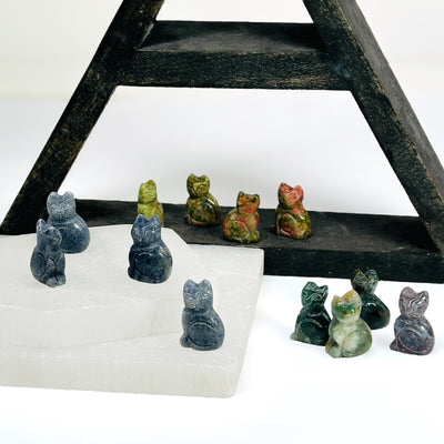 Gemstone Cats on a white table with a dark wood shelf and 2 selenite slabs.