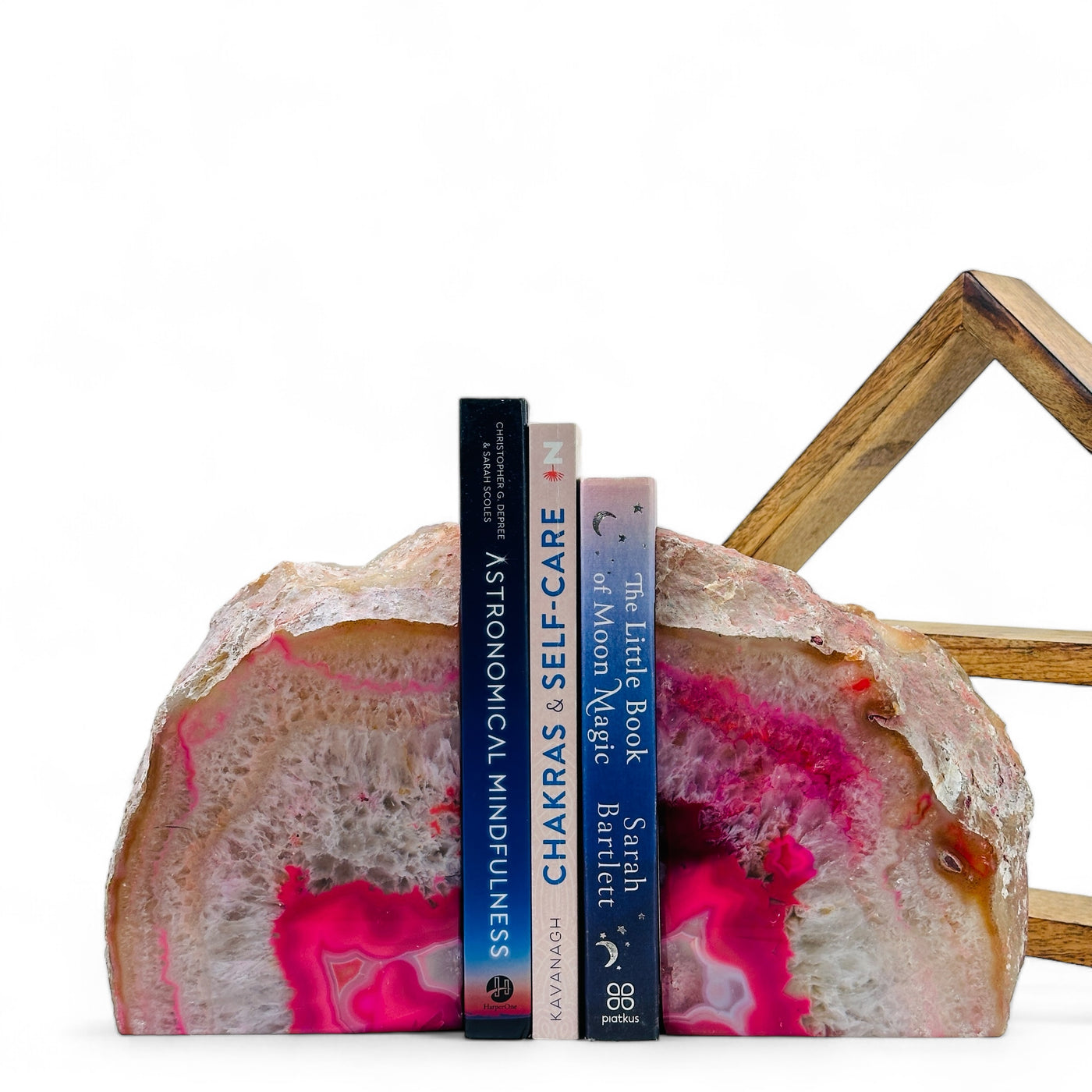 Large Pink Dyed Agate Bookend with three books in between in front of a wood shelf with a white background.