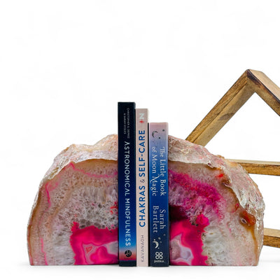 Large Pink Dyed Agate Bookend with three books in between in front of a wood shelf with a white background.