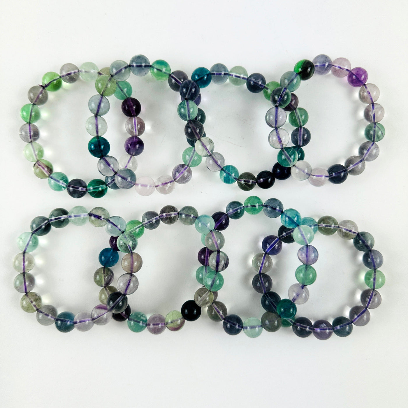 Rainbow Fluorite Round Bead Bracelets spread out on a table to show array of color