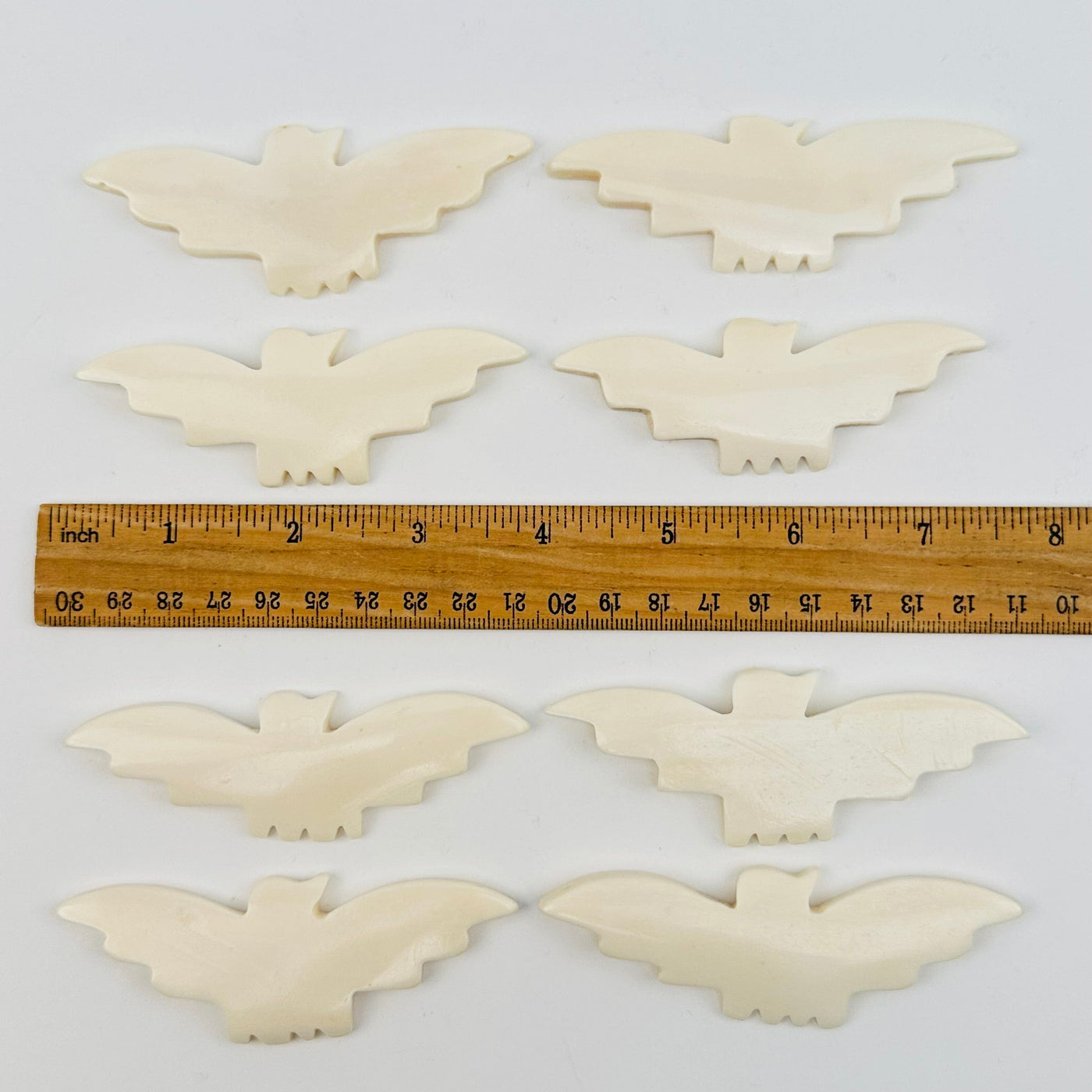 carved bone bats displayed next to a ruler for size reference 