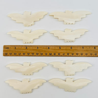 carved bone bats displayed next to a ruler for size reference 