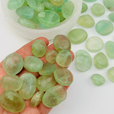 multiple tumbled fluorite stones in hand for size reference 