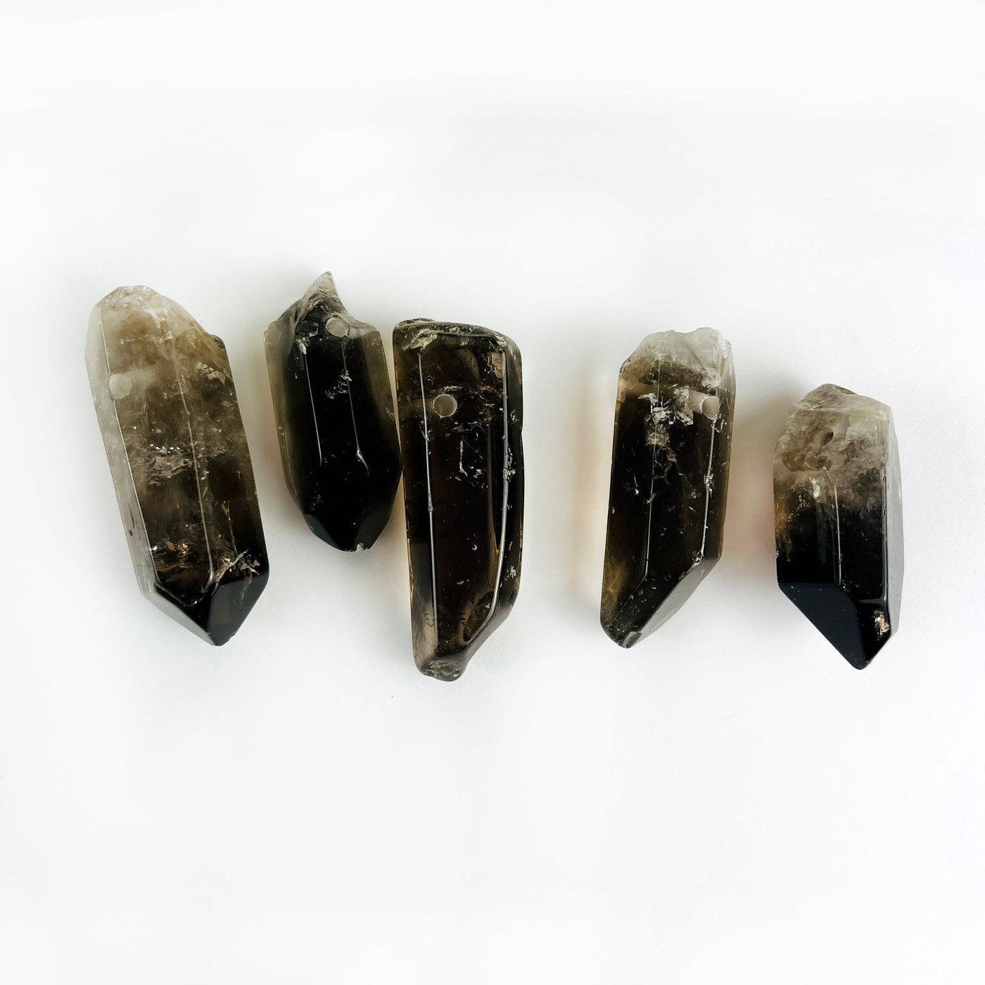5 Jumbo Smoky Quartz Crystal Polished Point Drilled Pendants on a table showing different sizes of stock available