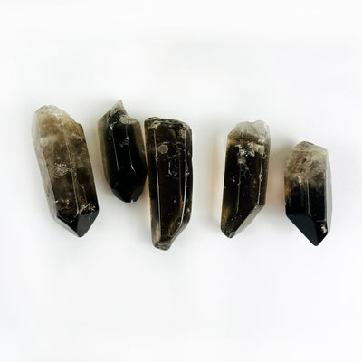 5 Jumbo Smoky Quartz Crystal Polished Point Drilled Pendants on a table showing different sizes of stock available
