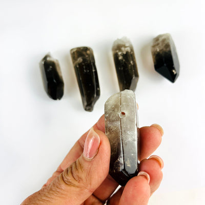 Jumbo Smoky Quartz Crystal Polished Point Drilled Pendants with one in a hand showing the drilled hole