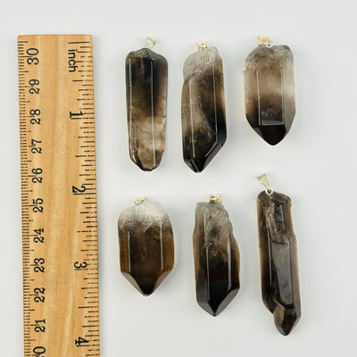 smokey quartz polished pendants displayed next to a ruler for size reference 