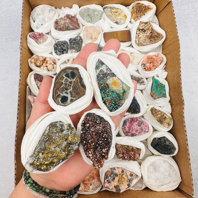 assorted minerals in a brown box with 4 held in a woman's hand.