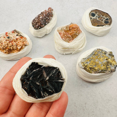 assorted minerals on a gray background and one held in a woman's hand showing it is about three fingers wide.