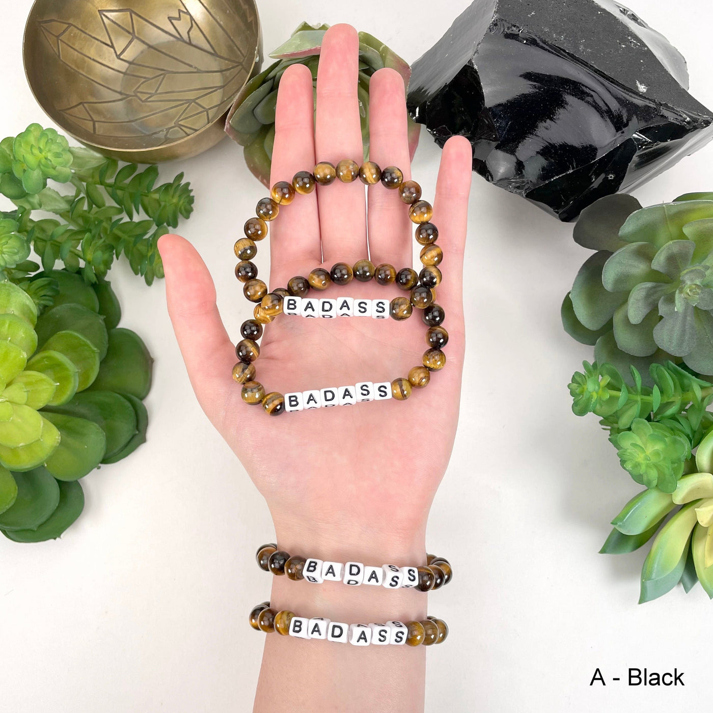 Black print "BADASS" letter bead option in hand and on wrist for color reference