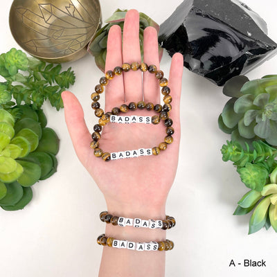 Black print "BADASS" letter bead option in hand and on wrist for color reference