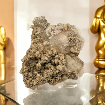 Giant Lodalite Quartz Cluster pictured on glass surface with gold statues in the background