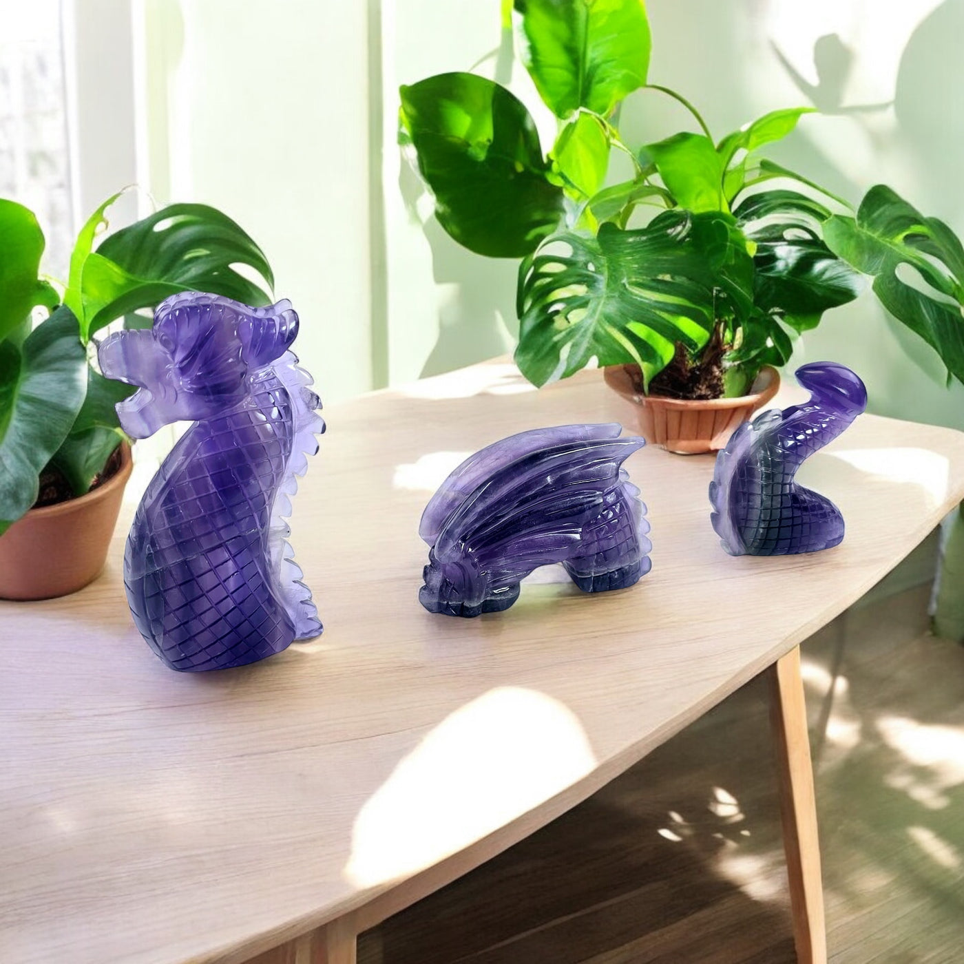 Purple Fluorite Crystal Dragon Carving on light wood table with plants in the background