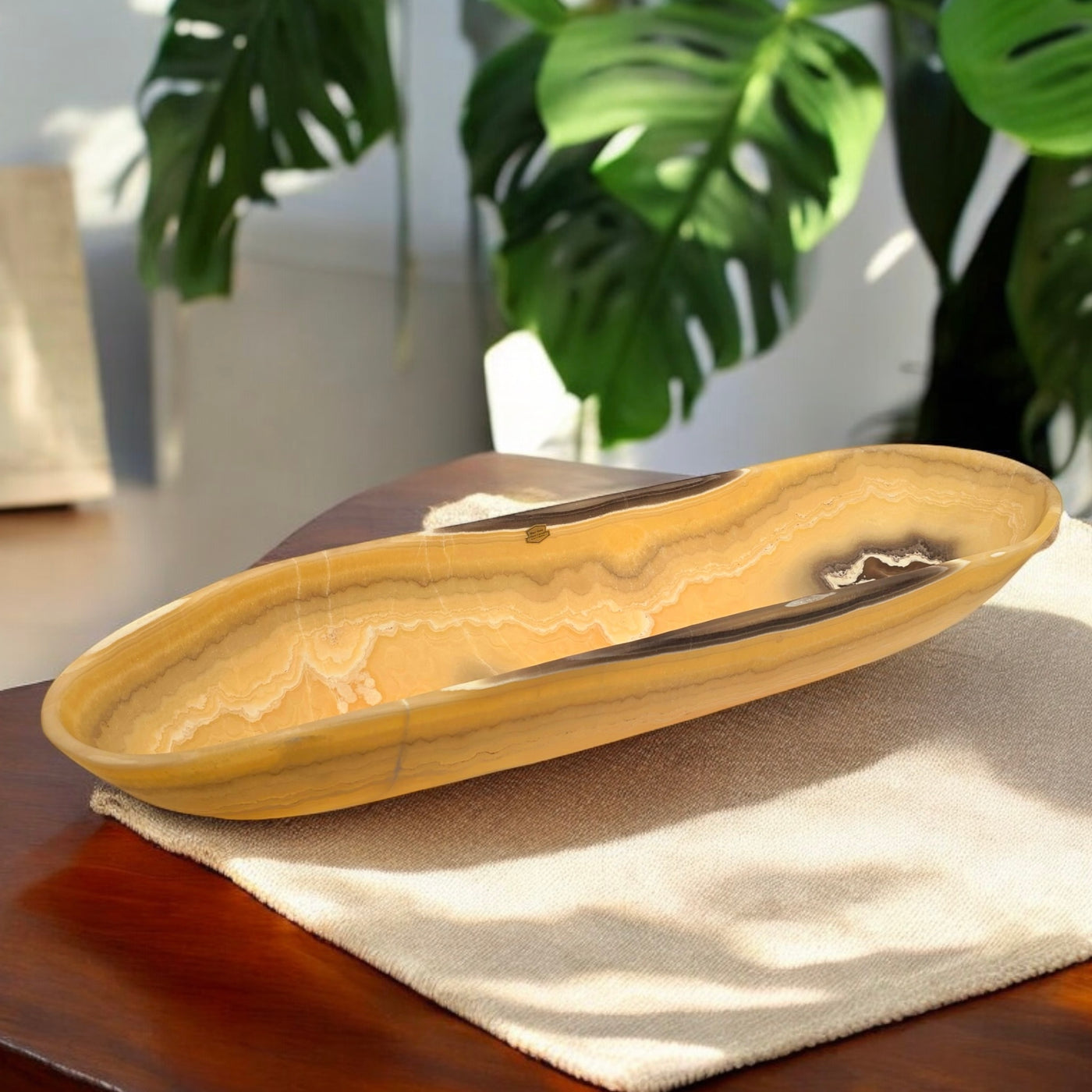 Mexican Onyx Long Freeform Crystal Bowl on table with beige mat with plants in the background