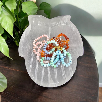 Selenite Hands Crystal Bowl top view with jewelry in hands bowl with plants and wooden table in the background