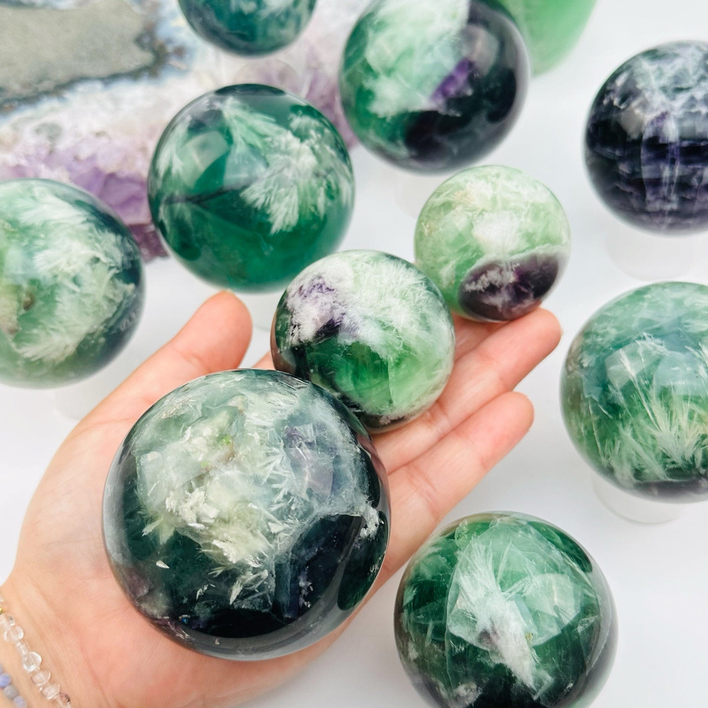 multiple feather fluorite crystal spheres in hand for size reference 