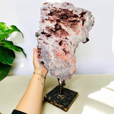 large pink amethyst crystal on metal stand next to hand for size reference 