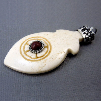 Tibetan Carved Bone Feather Pendant with Red Coral Gemstone and Silver Toned Brass Cap shown at an angle in white
