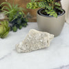 Crystal Quartz Cluster on marble table with green plants in background for reference.