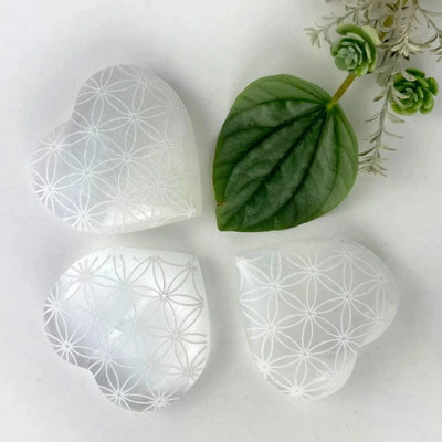 3 Selenite Crystal Stone Hearts, Engraved with Flower of Life Pattern on a table