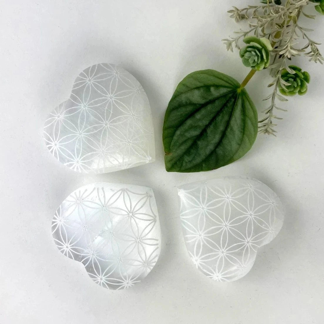3 Selenite Crystal Stone Hearts,  Engraved with Flower of Life Pattern on a table