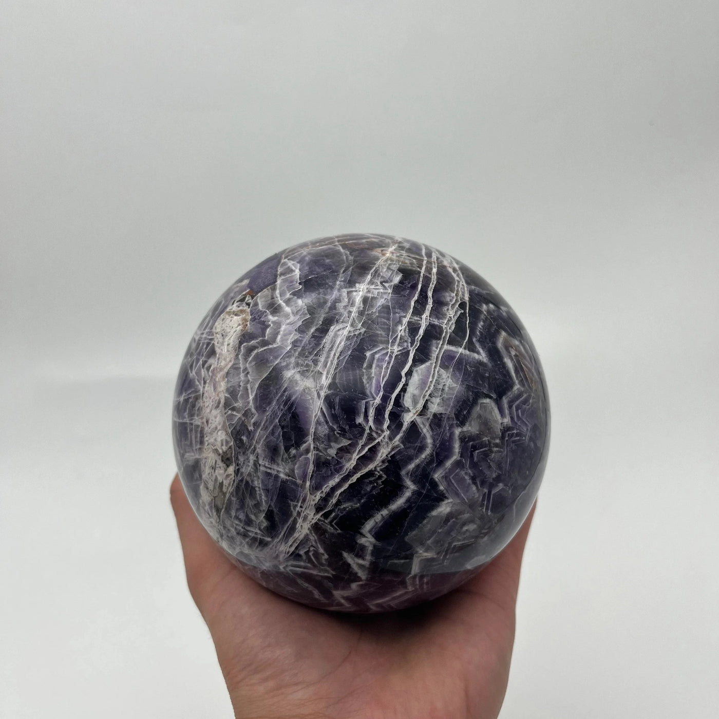 Chevron Amethyst Crystal Ball Sphere in a hand for size reference