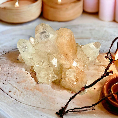 Peach Stilbite Crystal with Apophyllite on wooden table with peach candles in the background