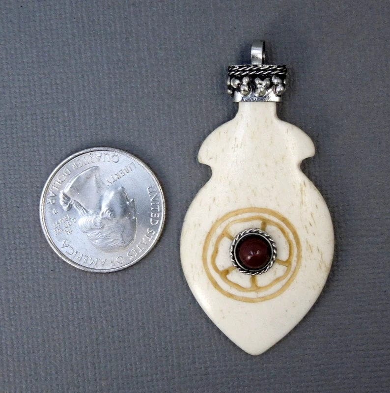 Tibetan Carved Bone Feather Pendant with Red Coral Gemstone and Silver Toned Brass Cap next to a quarter for size reference
