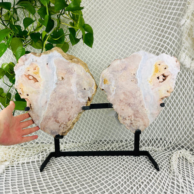 hand next to Pink amethyst double wings on metal stand with decorations in the background