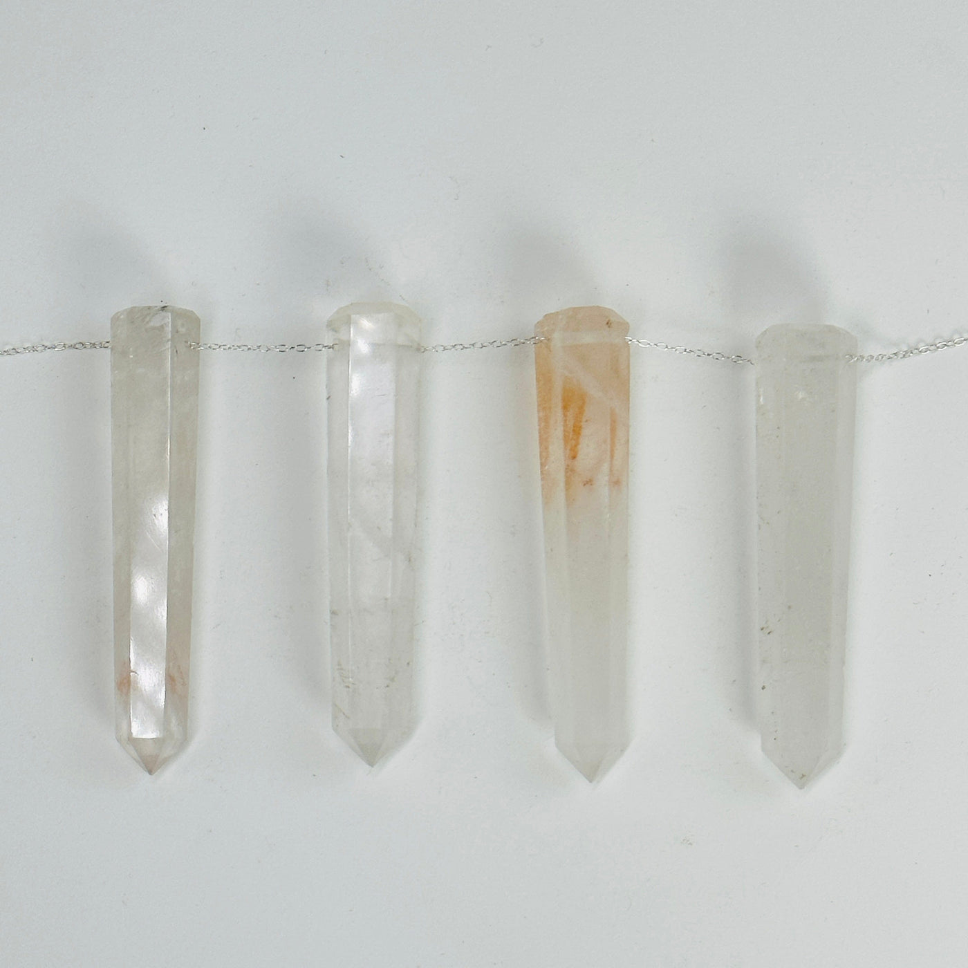 crystal quartz think obelisks drilled with a chain through them on white background