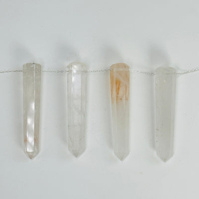 crystal quartz think obelisks drilled with a chain through them on white background