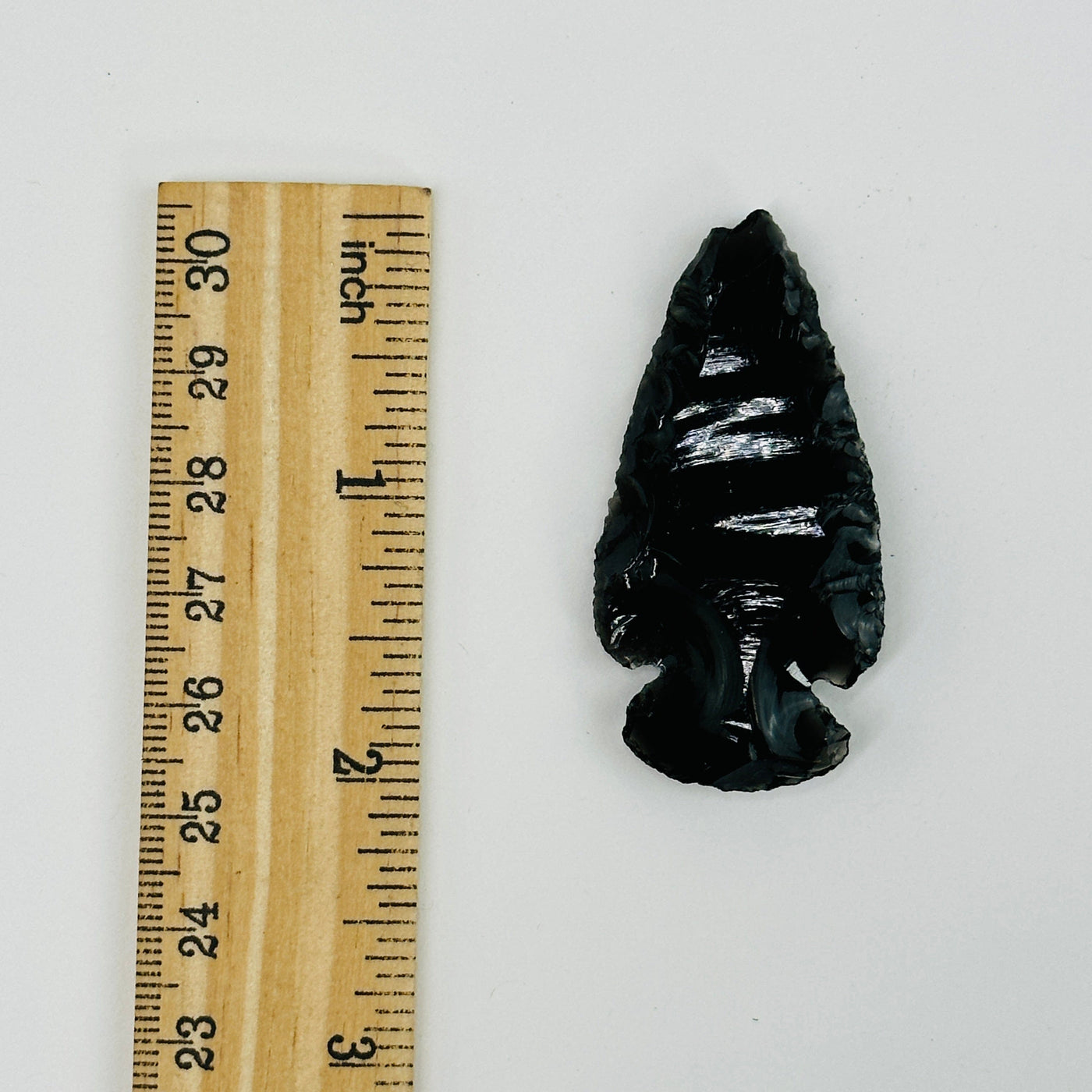 obsidian arrowhead next to a ruler for size reference