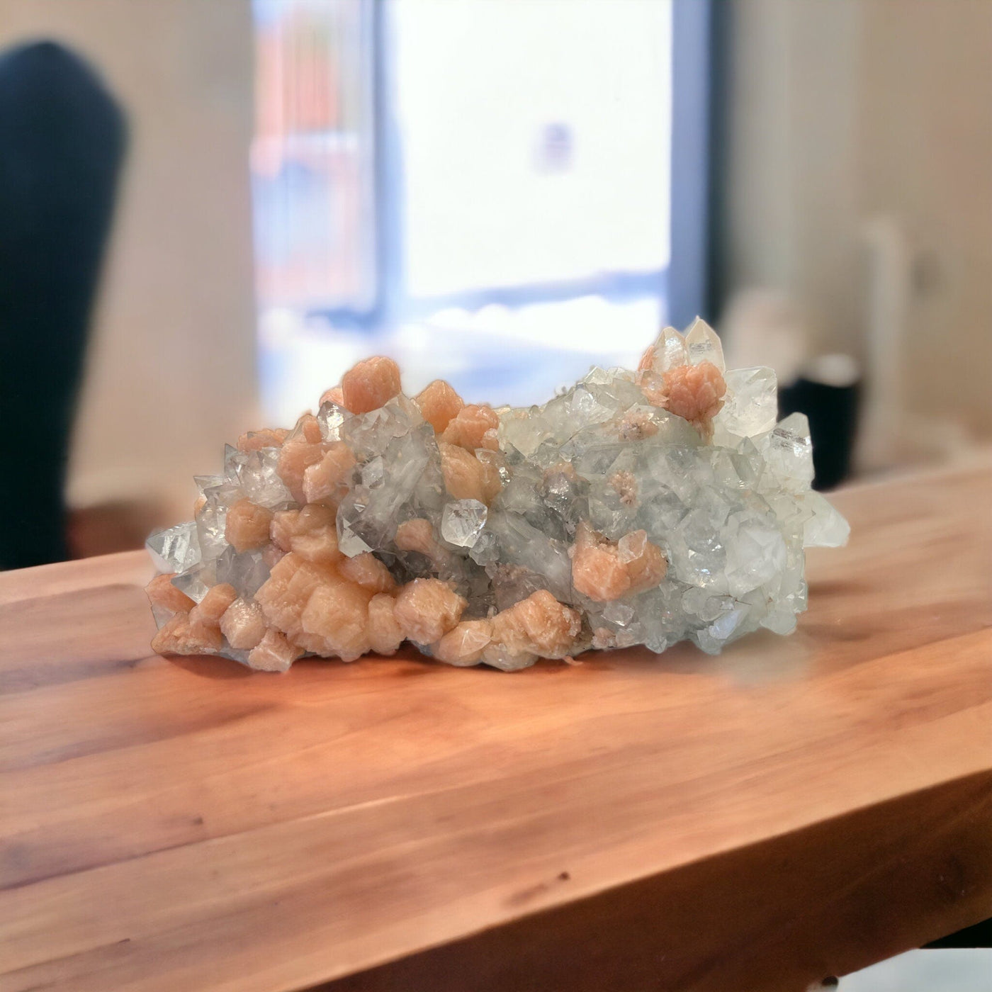 Large zeolite cluster with apophyllite and peach stillbite crystals on a wood counter.
