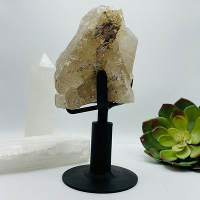 side view of Rutilated Crystal Quartz Cluster on Metal Stand with decorations in the background