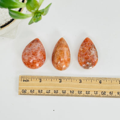 orchid calcite teardrop cabochons next to a ruler for size reference