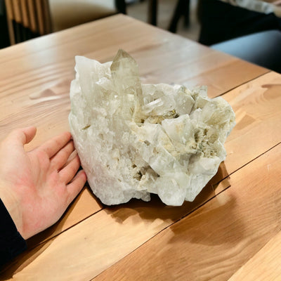 hand next to crystal quartz cluster on table
