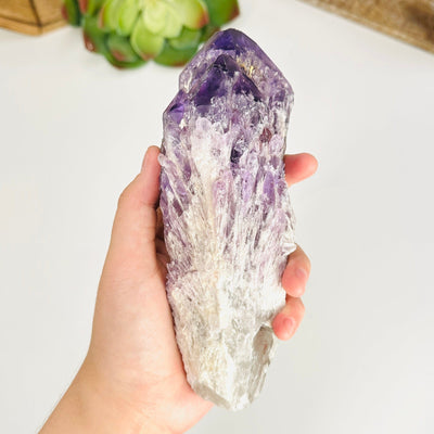 hand holding up amethyst cluster point with decorations in the background