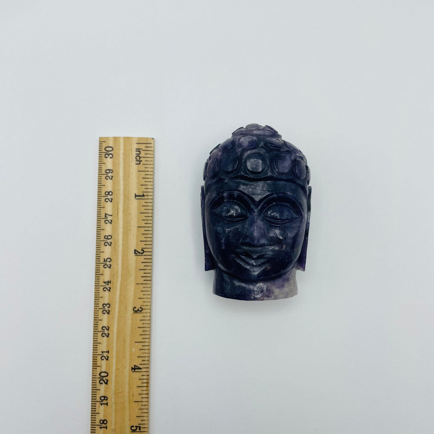 lepidolite Buddha head next to a ruler for size reference