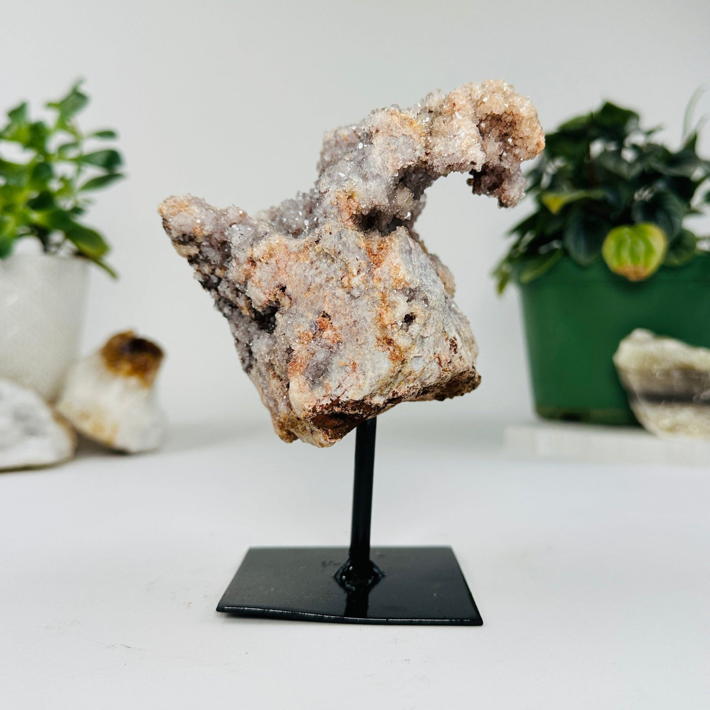 side view of raw pink amethyst on metal stand with decorations in the background