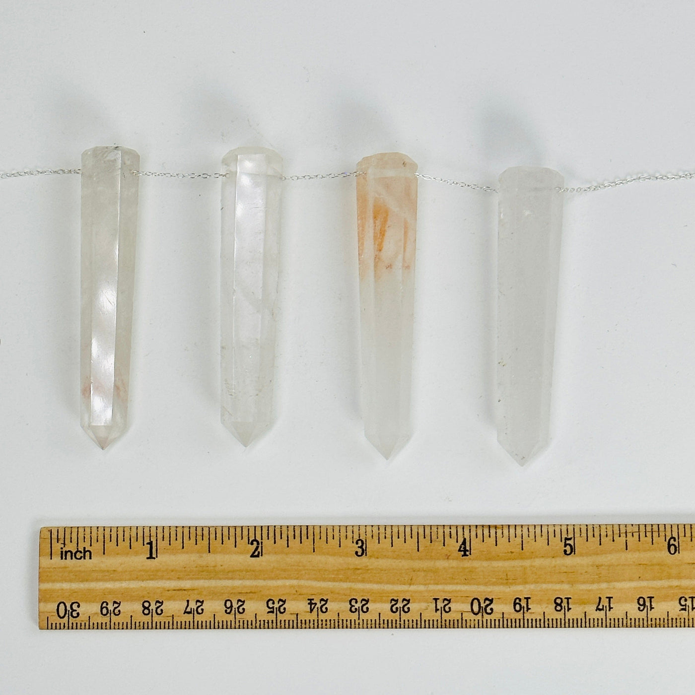 crystal quartz thin obelisks drilled with a chain through them next to a ruler for size reference