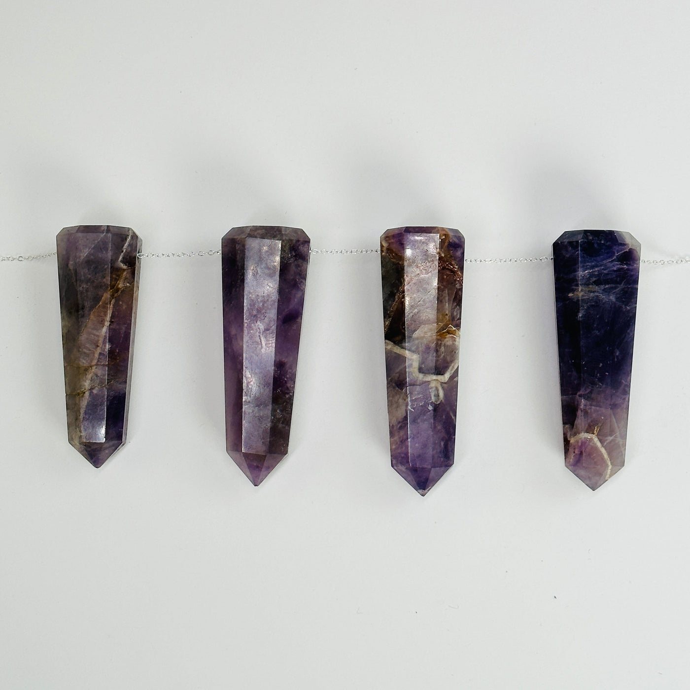 amethyst obelisk points with a chain through them on  white background