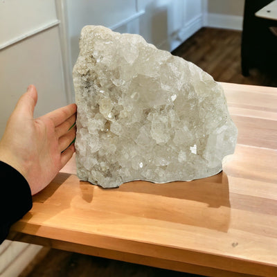 hand next to large crystal quartz cluster on a table