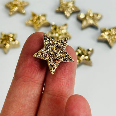 fingers holding up gold titanium druzy star with others in the background